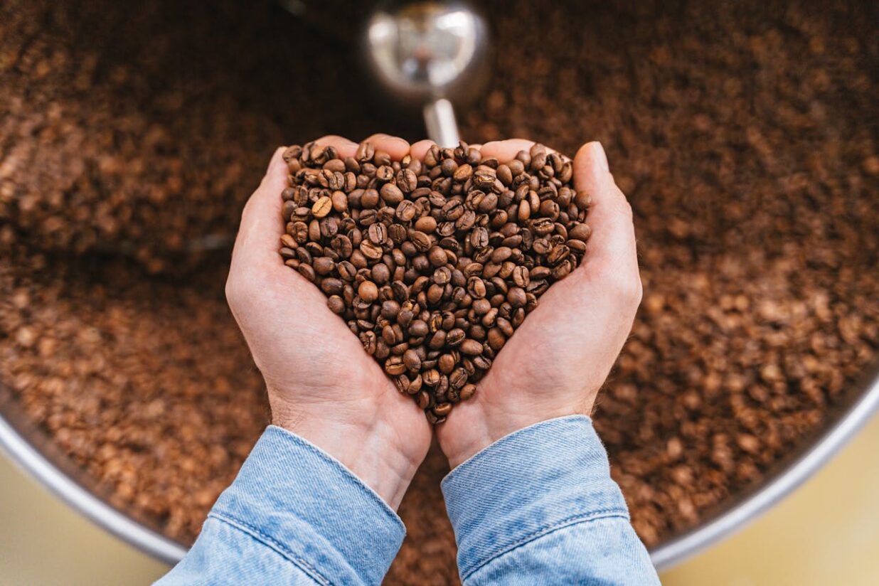 Close-up of hands holding heart-shaped roasted coffee beans, symbolizing love for coffee.